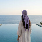 Person wearing a white dress and purple headscarf standing by an infinity pool with ocean view. Zawjien HeadScarf