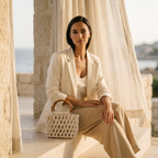ZAWJIEN Riviera Bag- Woman in a white outfit holding a woven handbag in an outdoor setting with columns and curtains.